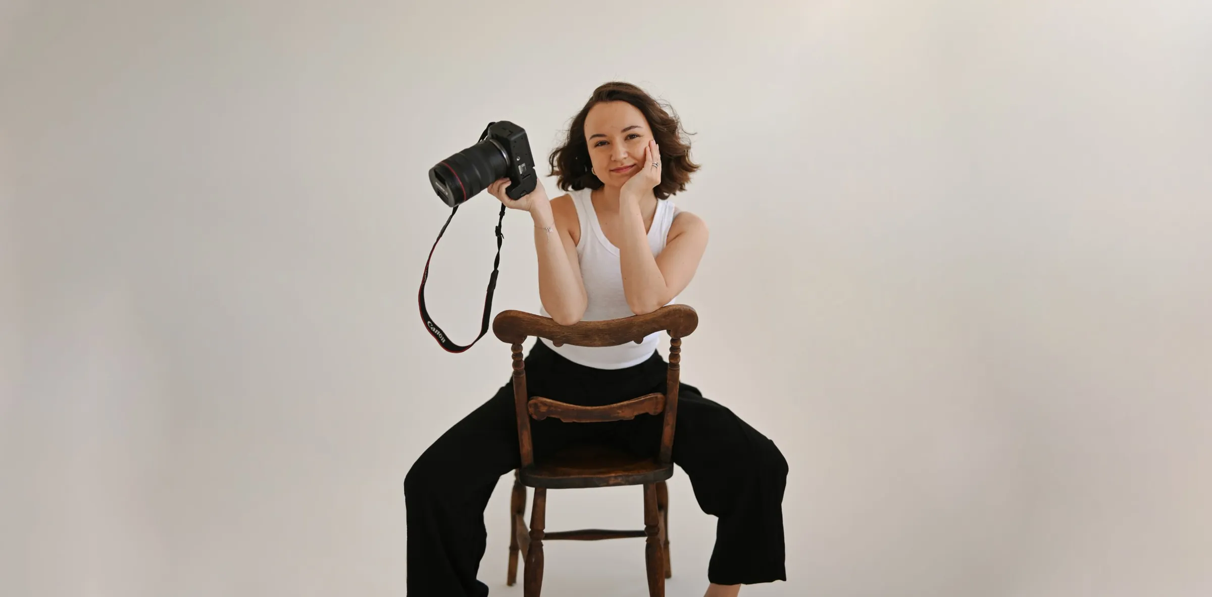 Lena Barber sitting on a wooden chair, holding her camera and smiling