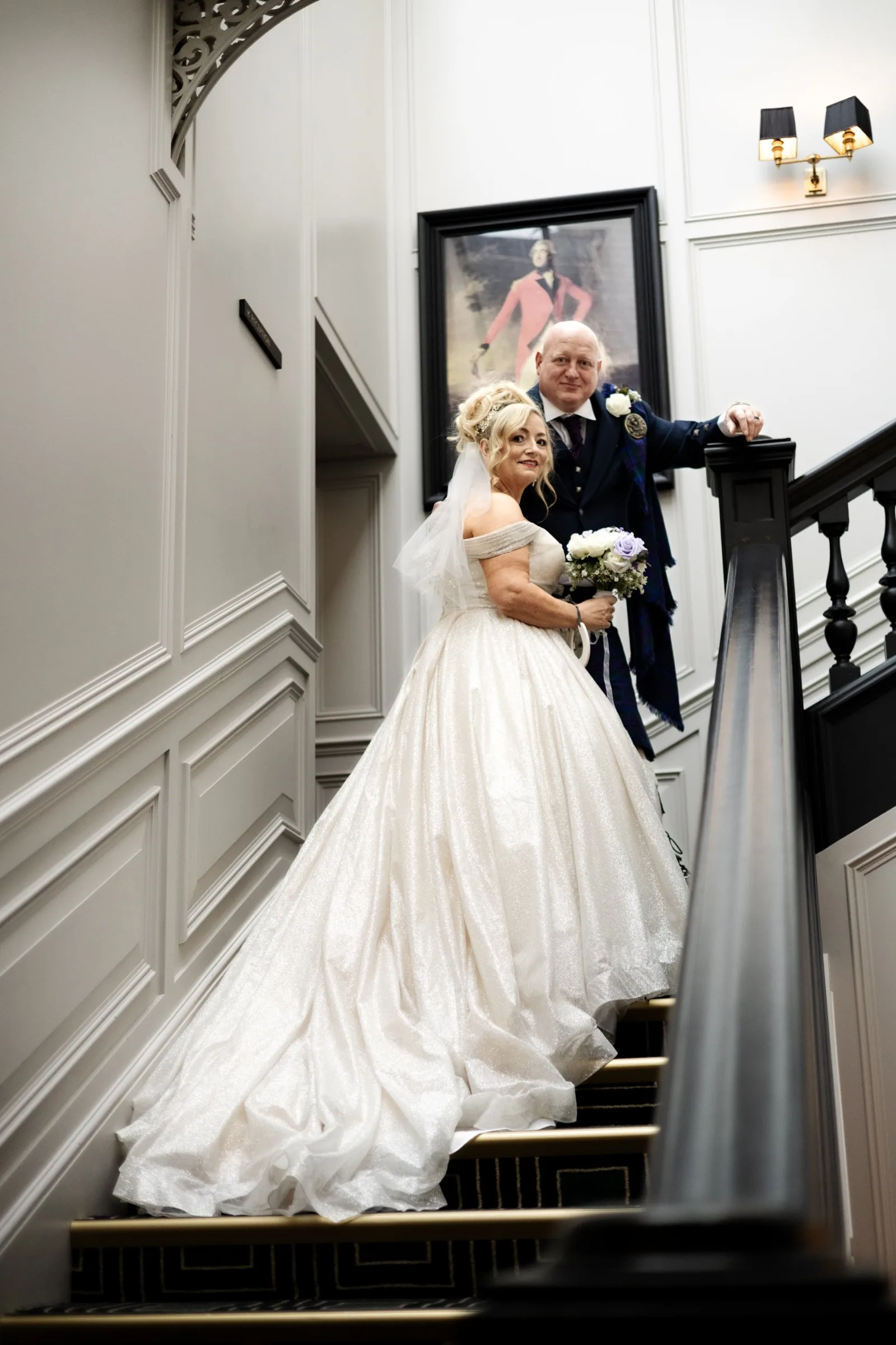 A bride in a sparkling ivory gown and her groom in a kilt on a grand staircase