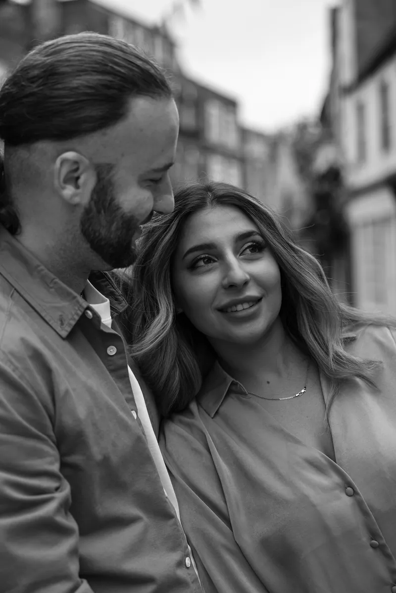 Black and white photograph of a couple smiling at each other on a town street