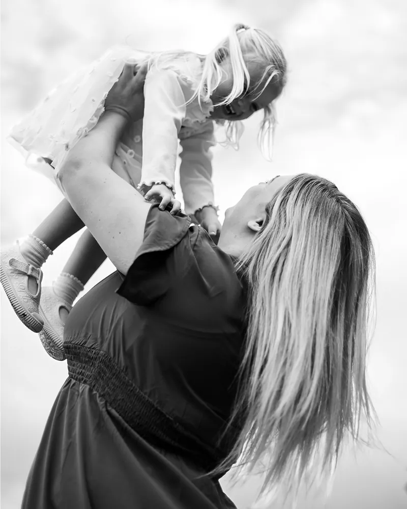Black and white photograph of a mother lifting her young daughter into the air